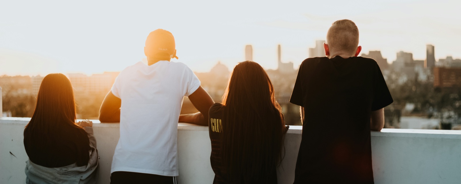 Four friends on a rooftop at sunset, looking out over a city skyline.