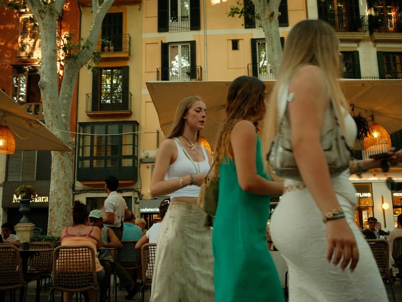 Three friends walking past outdoor café tables on a warm evening.