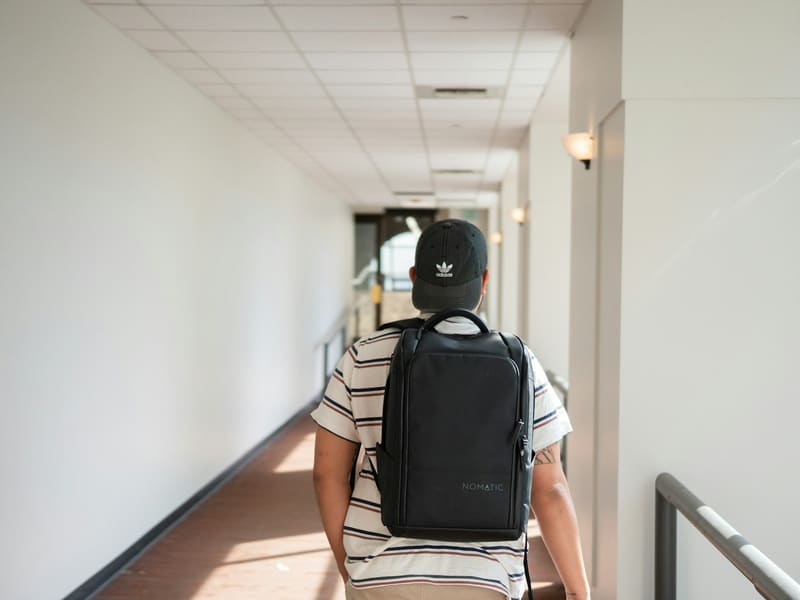 A traveller with a backpack walking down a bright hotel corridor.